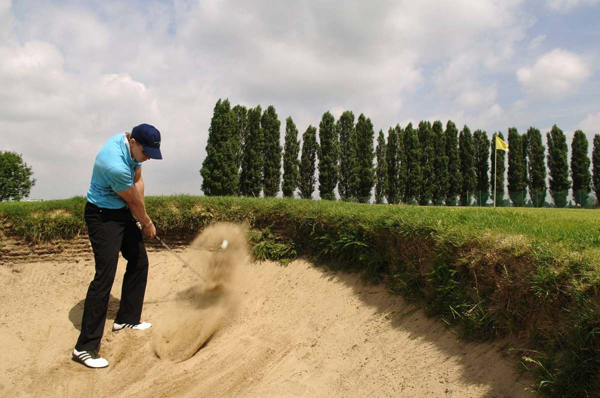 A golfer chipping out of a sand bunker